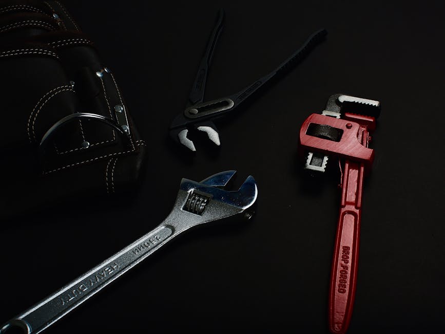 Close-up of various hand tools including wrenches and pliers on a dark surface.
