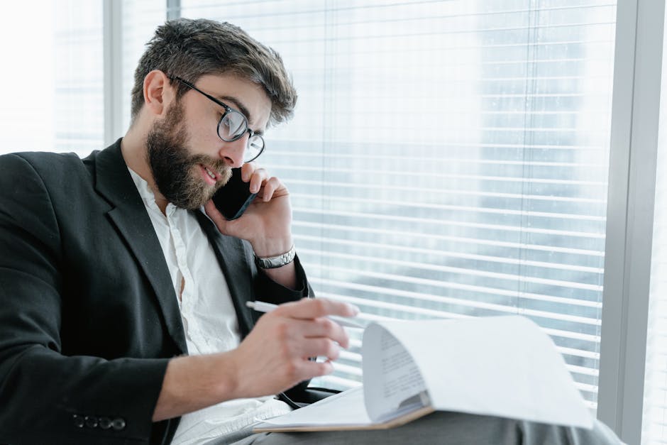 Businessman in glasses making a phone call while reviewing documents in a modern office setting.